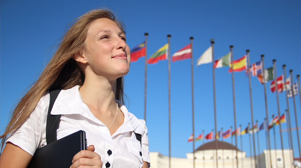 A student stands outside with international flags on flag poles in the background.